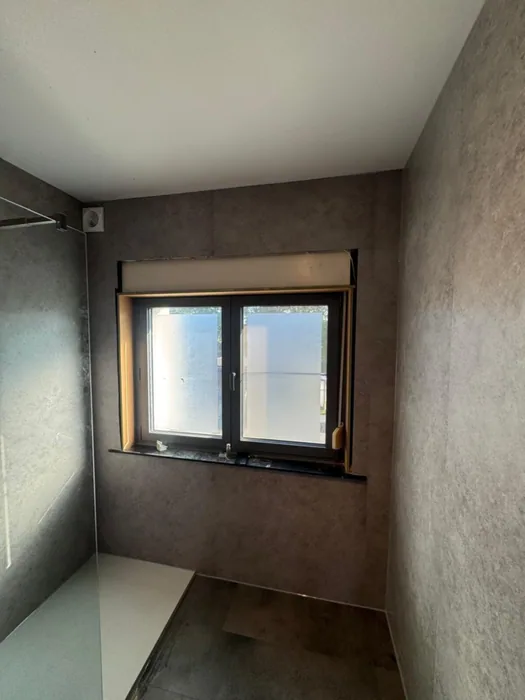 Badkamer met grijze steenlook wandpanelen, raam en inloopdouche