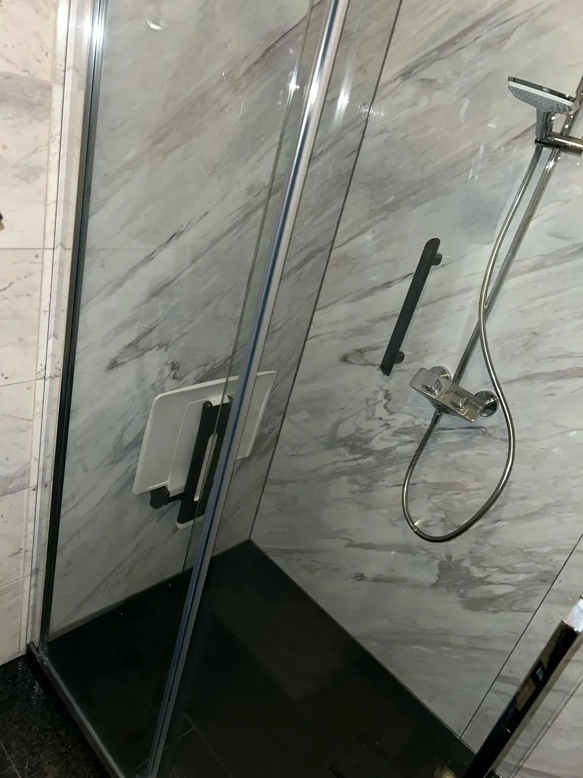 Douche met grijswit marmerlook wandpanelen, zwarte steunbeugel, opklapzitje en glazen wand