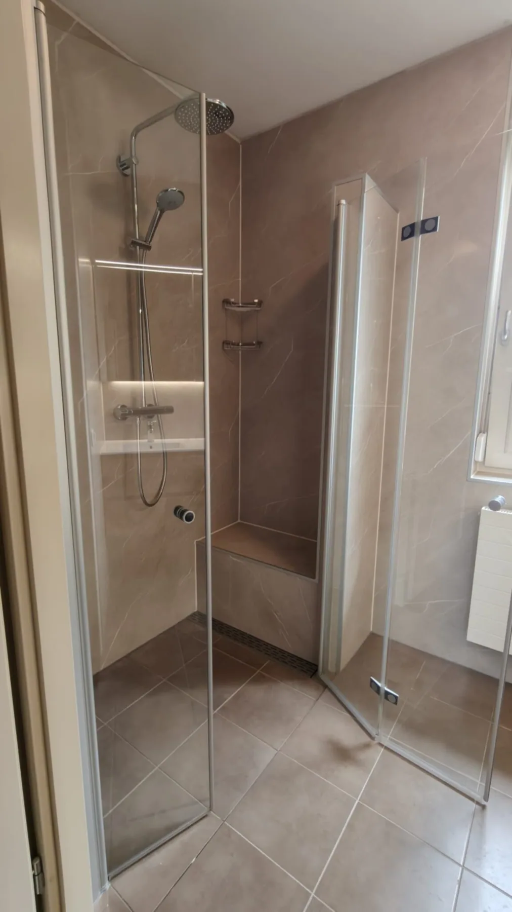 Douche met glazen vouwdeuren, regendouche, nis en zitbankje, beige marmerlook wandpanelen