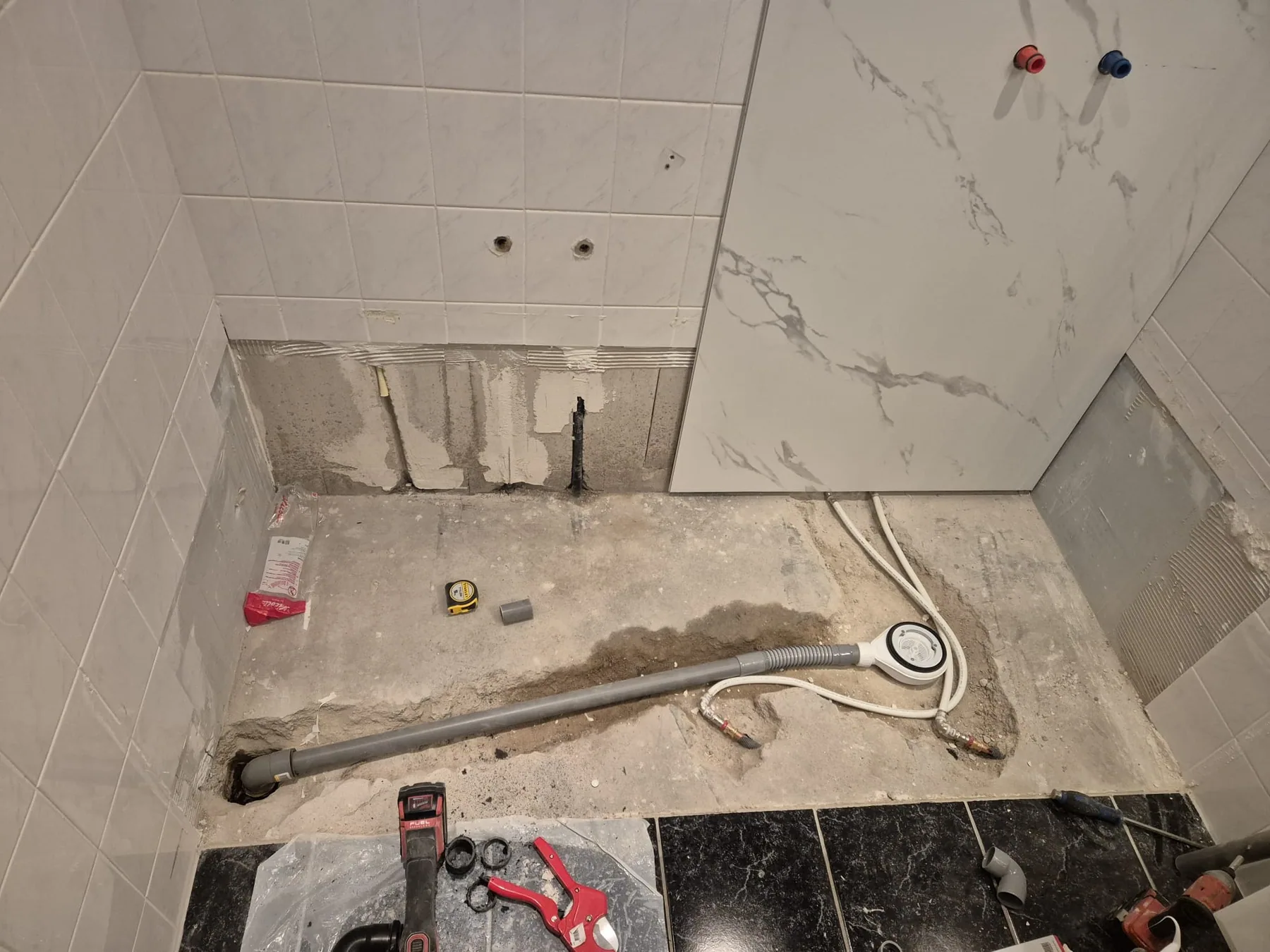 Douchehoek tijdens montage van marmerlook wandpanelen, afvoer en leidingen op de kale vloer