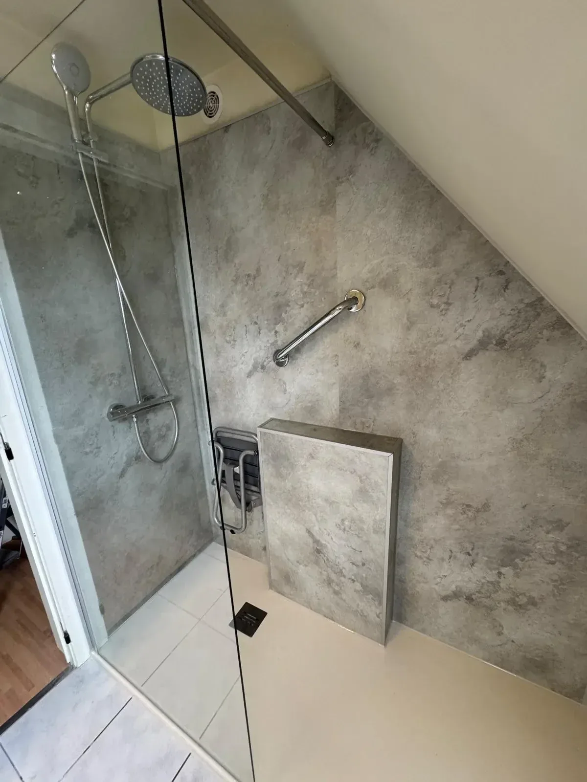 Douchehoek met grijze steenlook wandpanelen, thermostaatkraan, steunbeugel en opklapbaar douchezitje