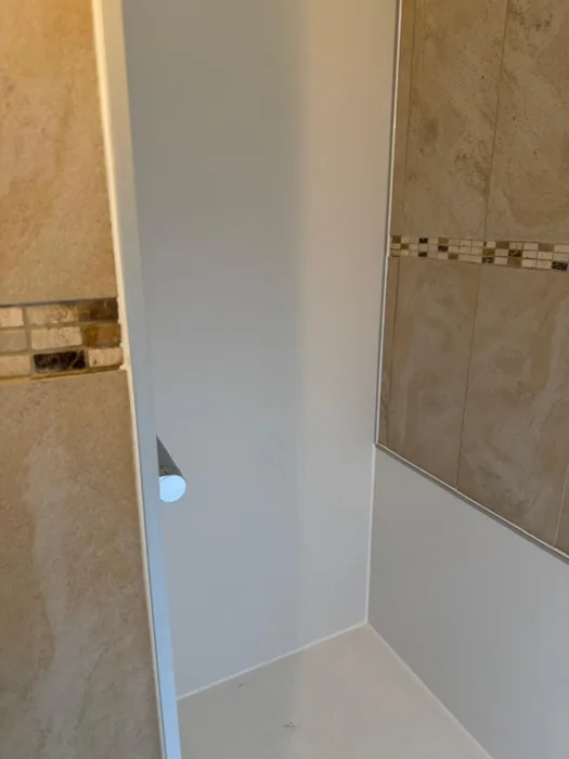 Nieuwe witte wandpanelen en douchevloer in een douchenis naast bestaande beige tegels met mozaïekrand