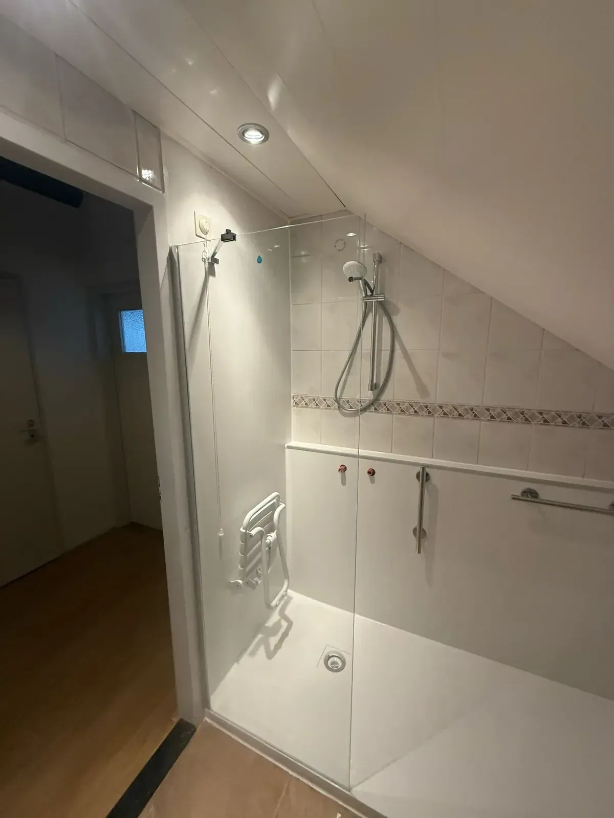Glazen douchedeur en witte panelen in zolderbadkamer met douchezitje