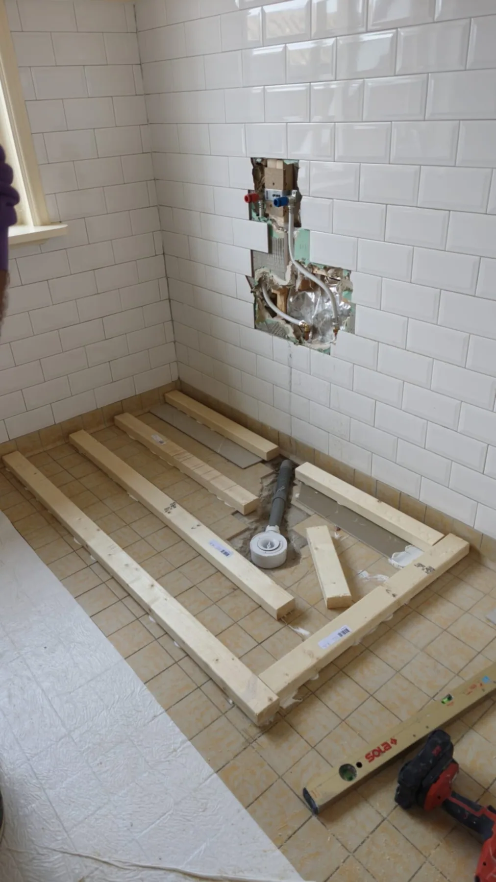Houten frame voor douchebak met afvoer en waterpas, metrotegels en inbouwkraan erachter