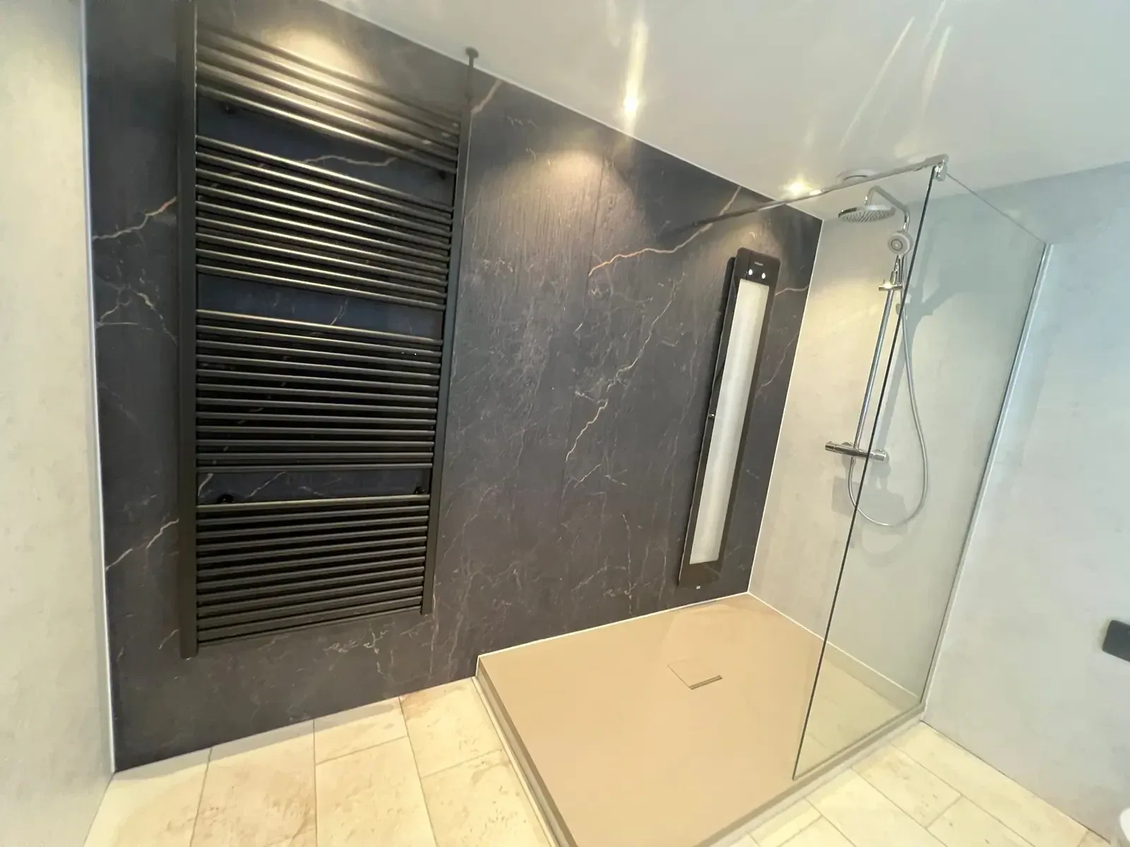 Inloopdouche met glazen wand naast donkere marmerlook wandpanelen en zwarte designradiator