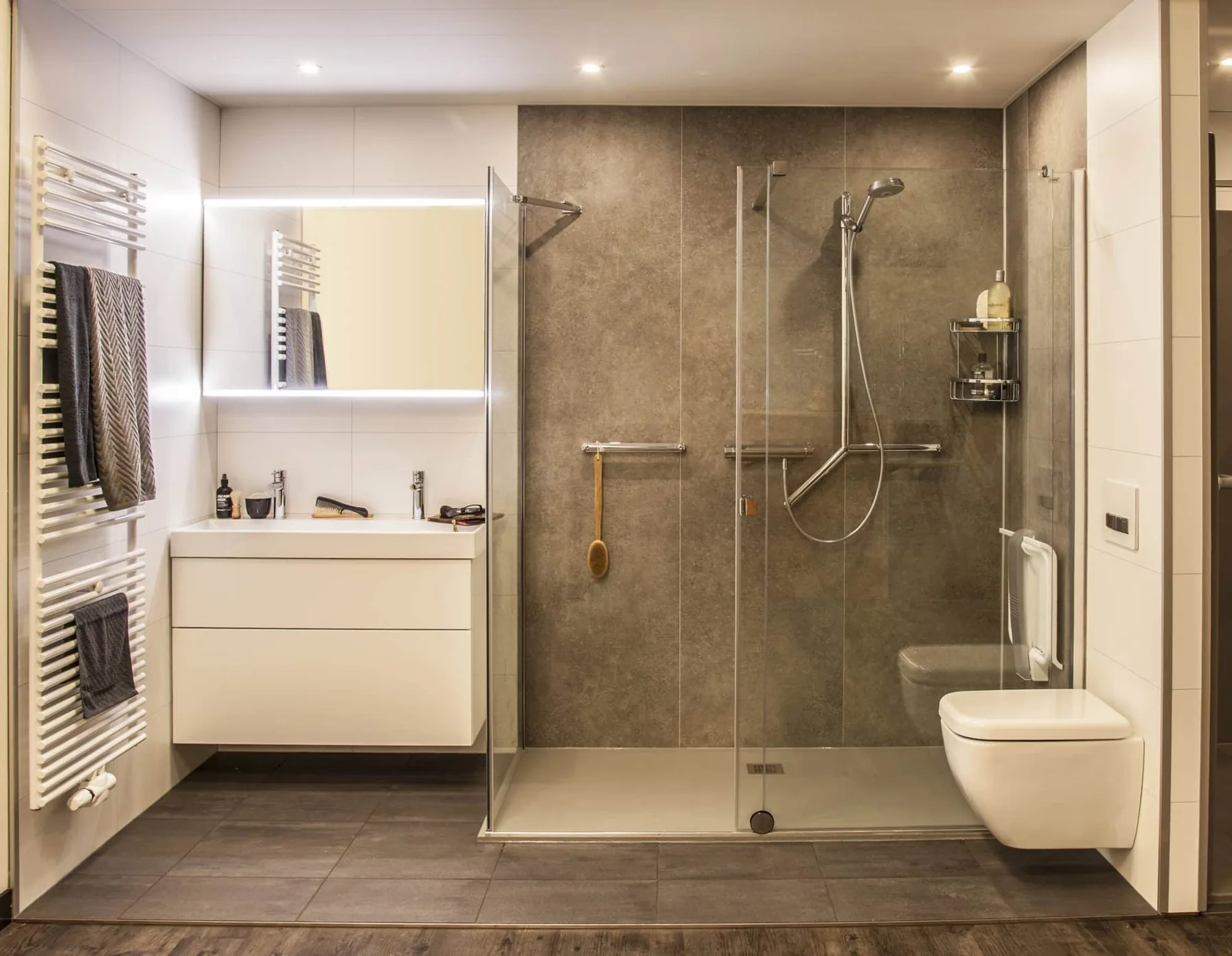 Badkamer met grote inloopdouche, steunbeugels, hangtoilet, wastafelmeubel en betonlook wanden