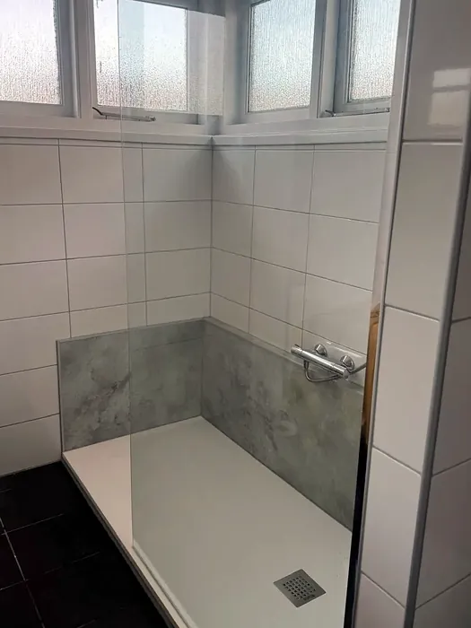 Douche met glazen schuifdeur naast een raam, grijs badmeubel met ledspiegel