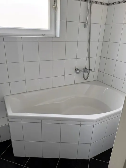 Voor: hoekbad met witte tegels onder het raam